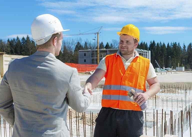 Mann im Anzug gratuliert Mann mit Helm und Warnweste