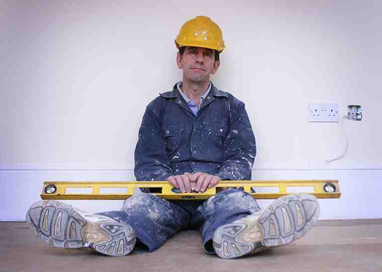 Handwerker mit Helm und Wasserwaage sitzt am Boden