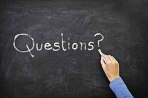 Hand schreibt mit Kreide Questions auf Tafel